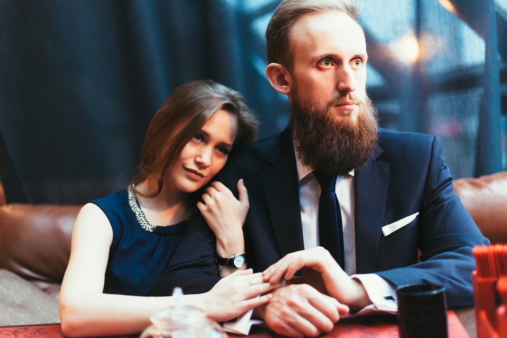 a lady is clinging to her partners arm and the male partner looks bored and unhappy