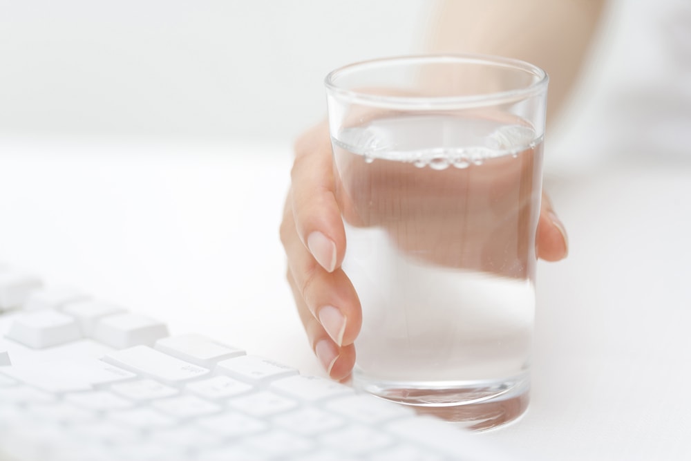This is a photo of a ladies hand holding a glass of water beside her keyboard