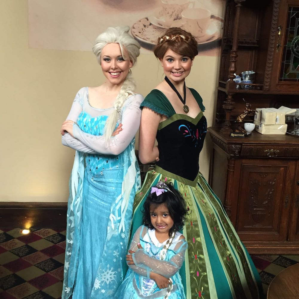 This is a photo of a little girl dressed as a princess with Anna and Elsa from Frozen