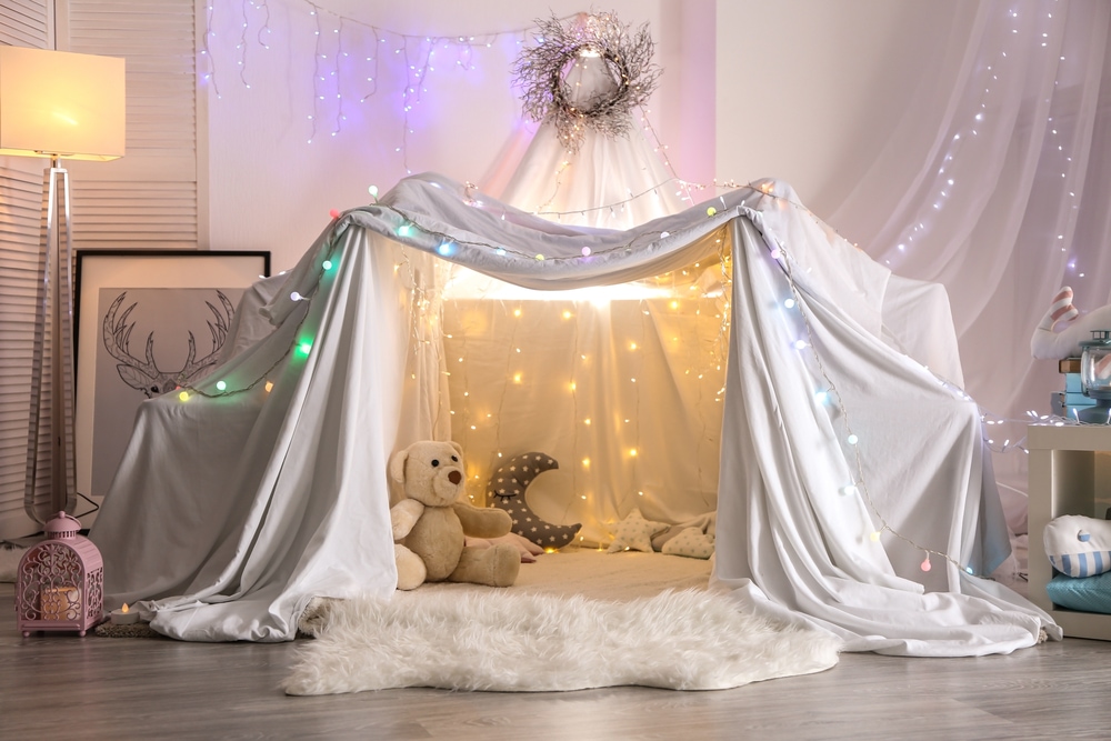 This is photo of a blanket fort with fairy lights and cushions