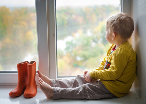 A child looks out of the rainy window