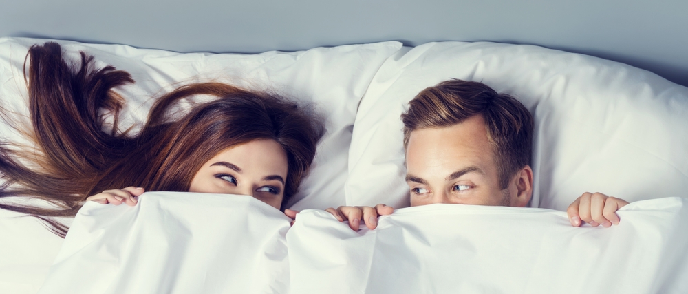 This is photo of people under covers looking at each other cheekily