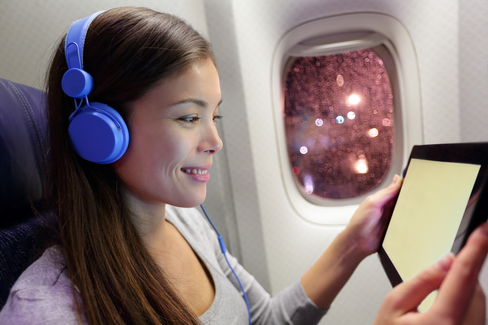 This is a photo of a woman looking at a tablet with her headphone on while on a plane