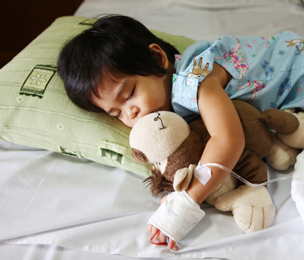 Young child cuddles monkey toy in hospital while sleeping