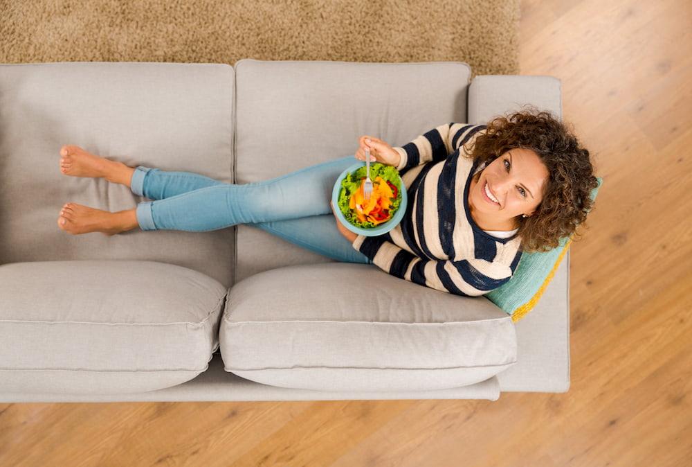 woman-eating-salad-on-sofa-min