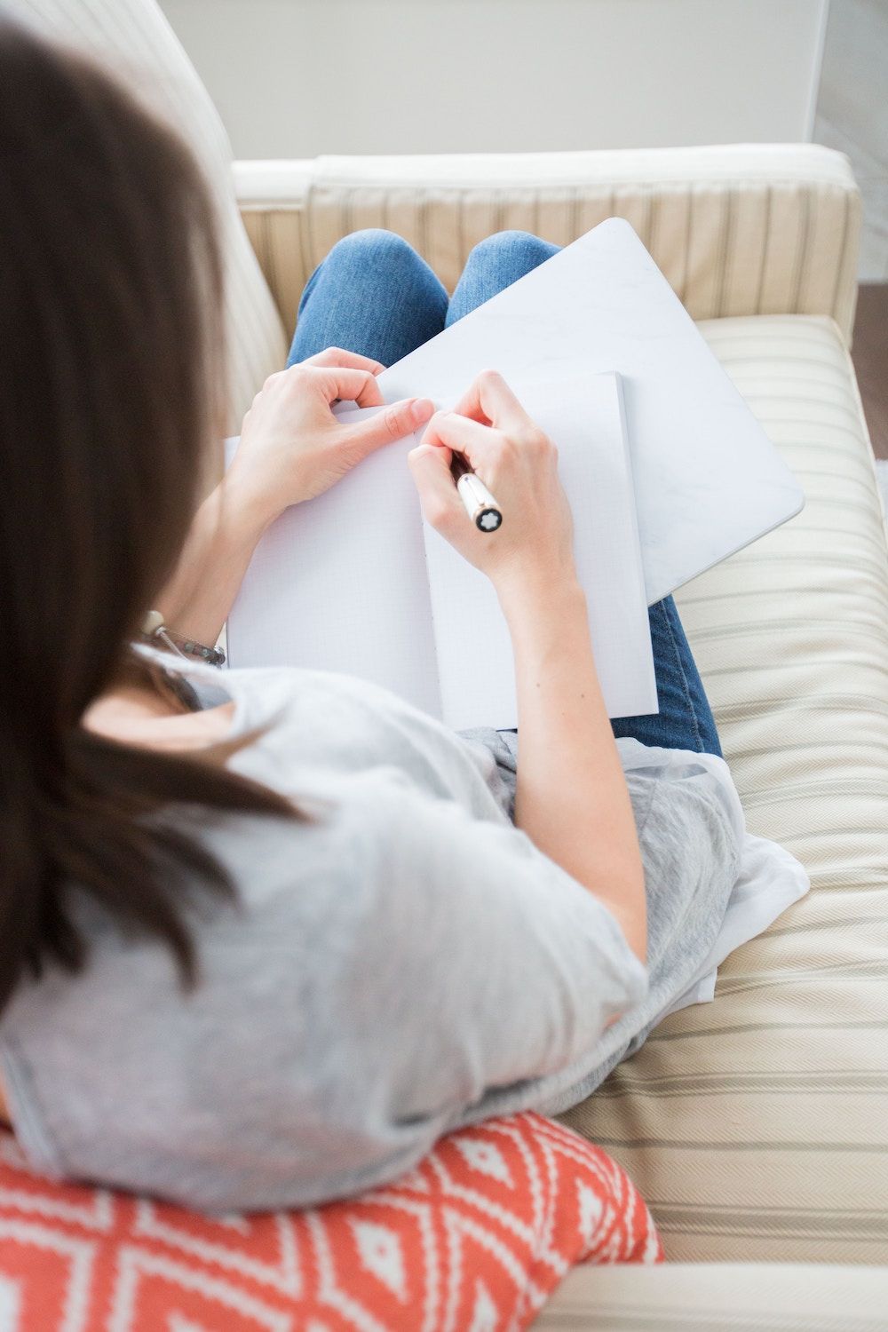 lady with brunette hair sitting on sofa and writing in note pad