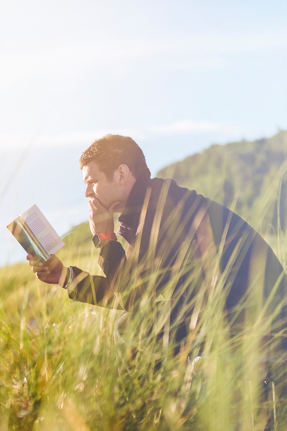 man sitting on a bench outside reading a book