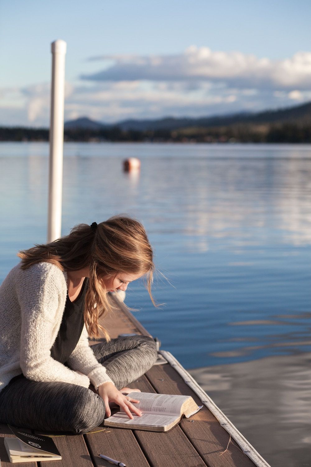 woman sitting outside by a lake reading a book