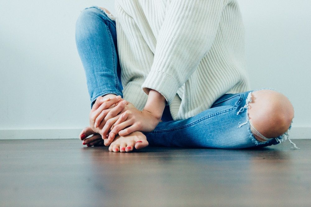 woman in white knitted jumper and blue denim jeans sitting on the floor with legs crossed