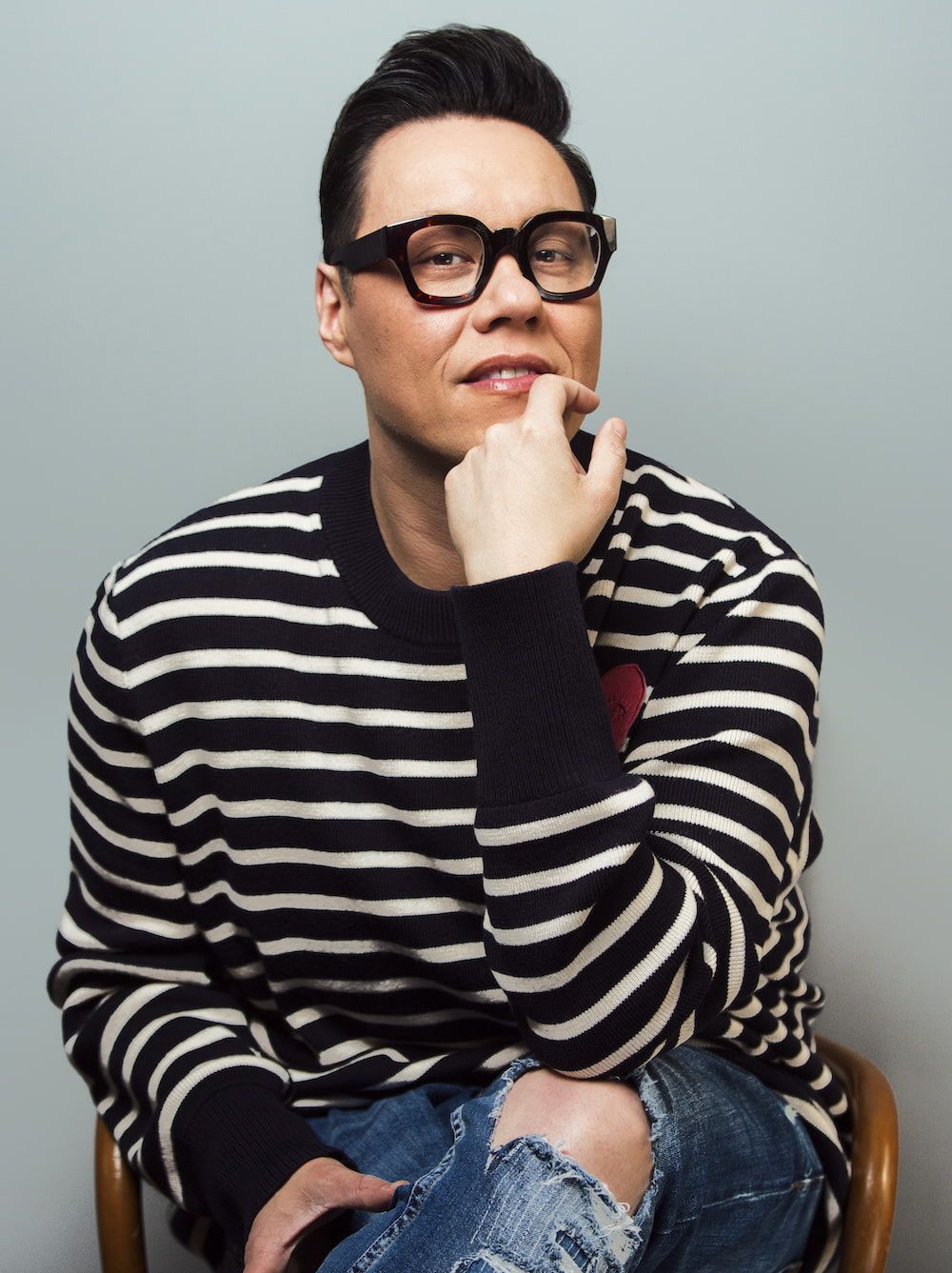 Gok Wan sitting in a chair with his chin resting on his hand