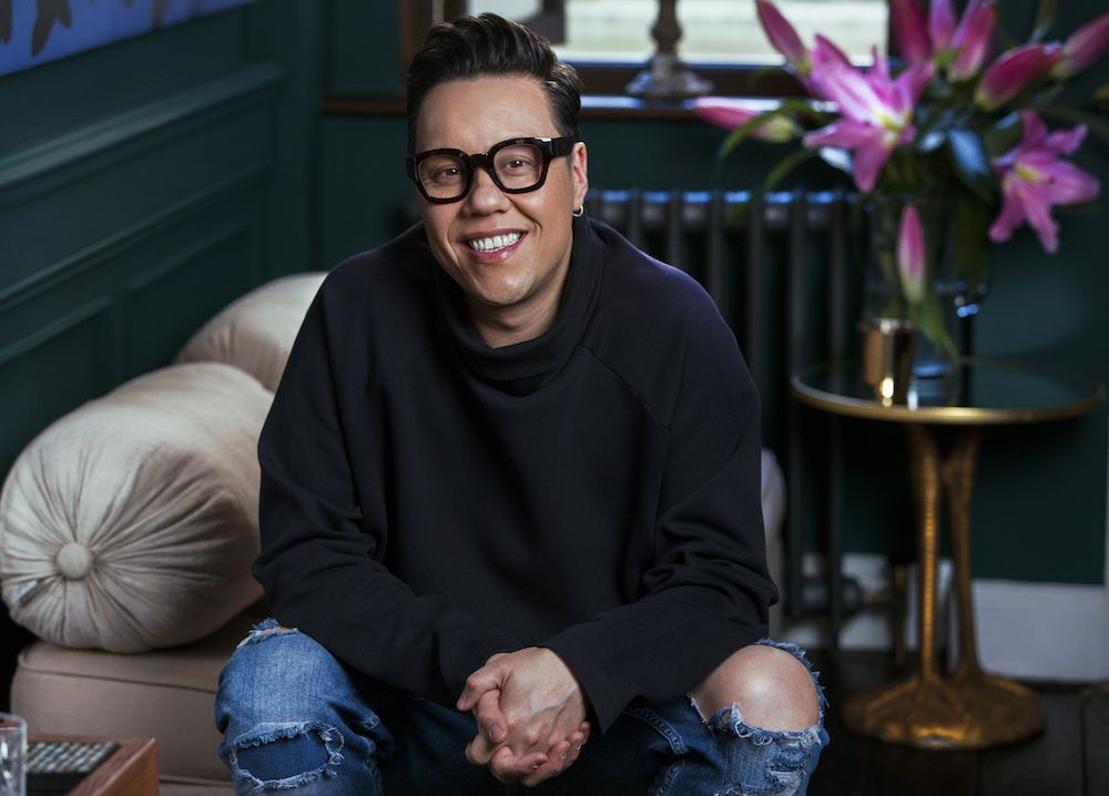 Gok Wan smiling at the camera, wearing a black roll neck jumper and ripped jeans