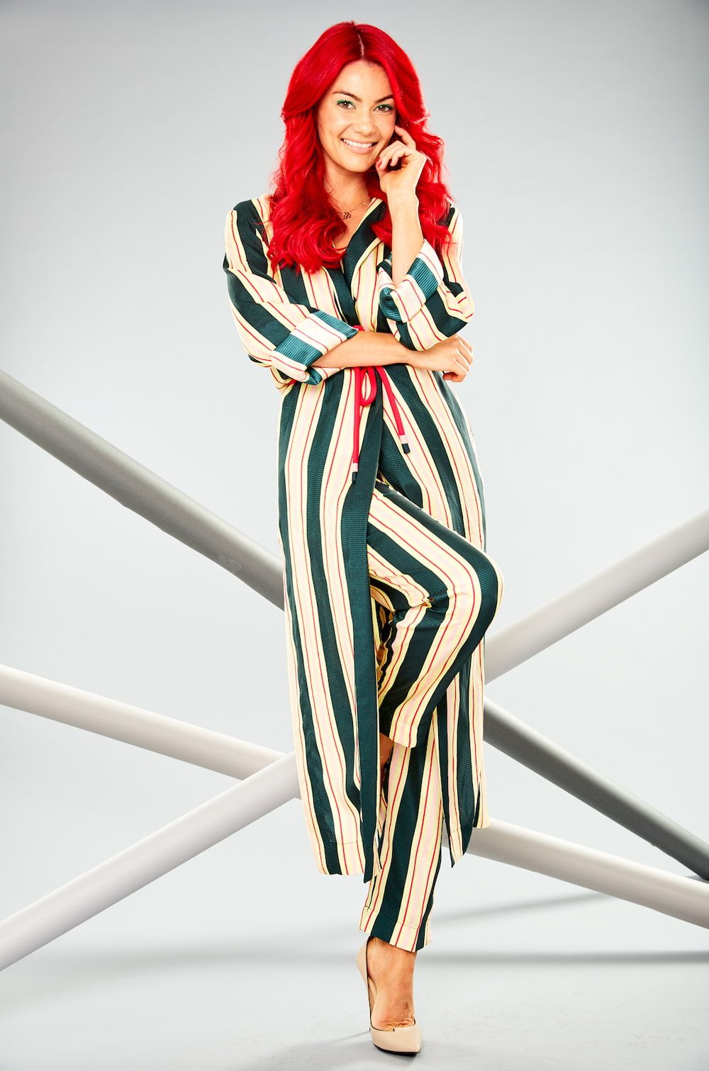 Dianne Buswell wearing a striped two piece, standing with one leg raised across the other
