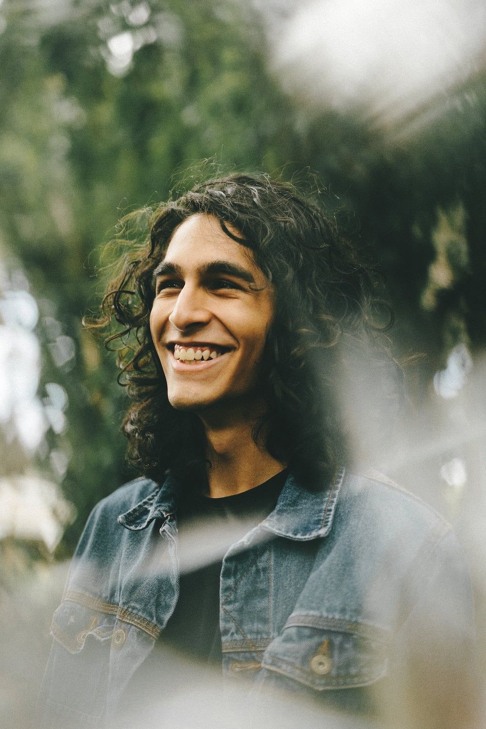 man with long dark curly hair smiling