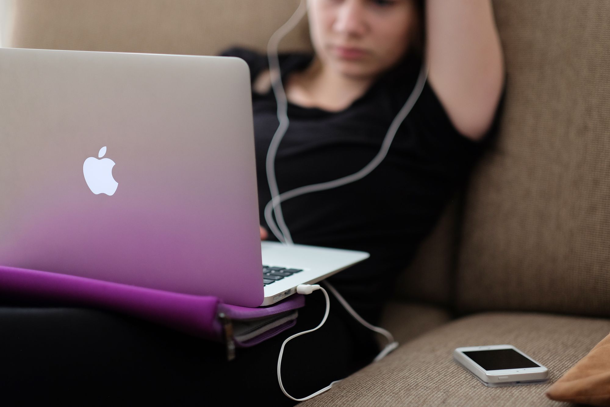A teen sits alone on the sofa, watching porn on her laptop with her headphones in.