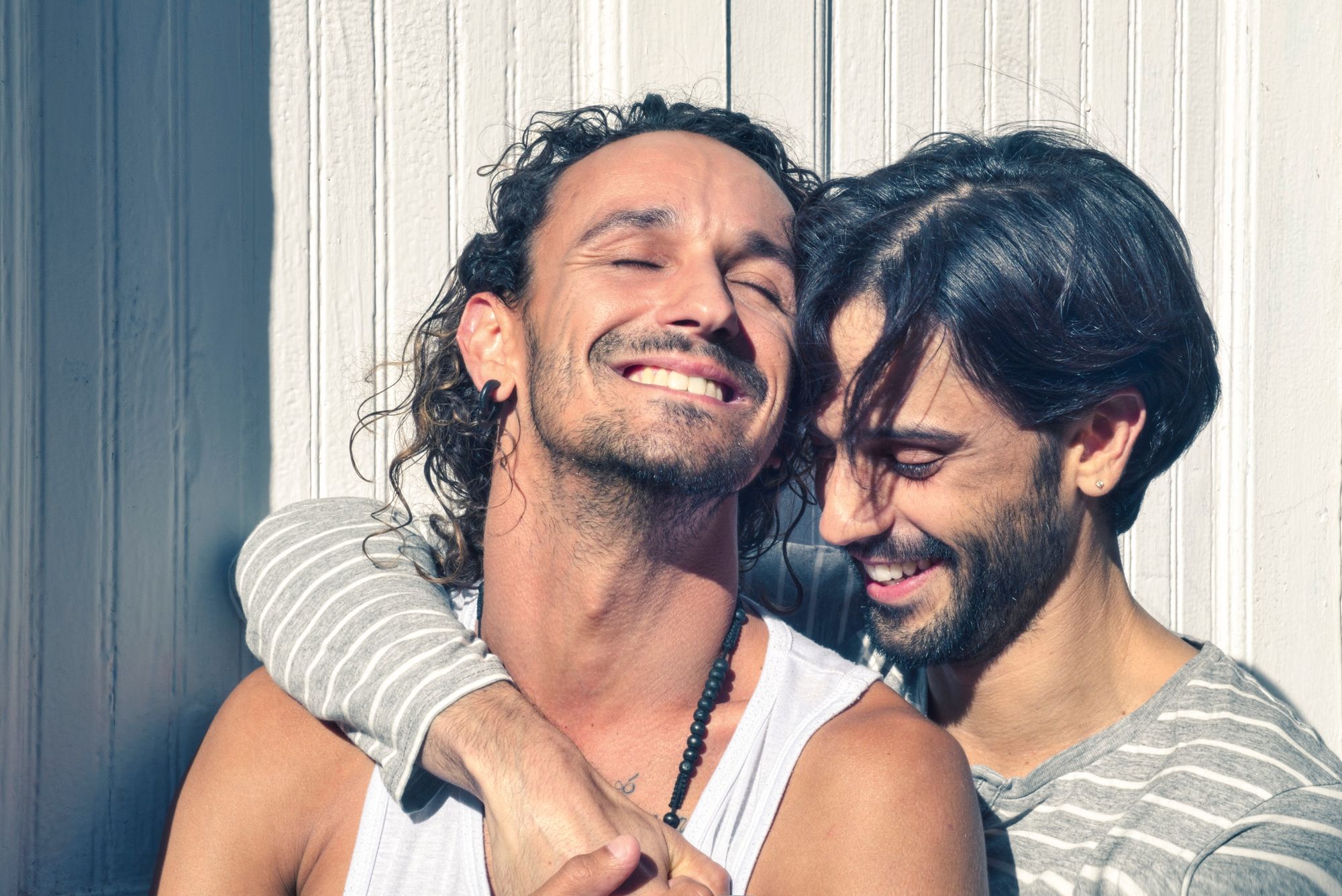 A gay couple embrace each other, smiling in the sun