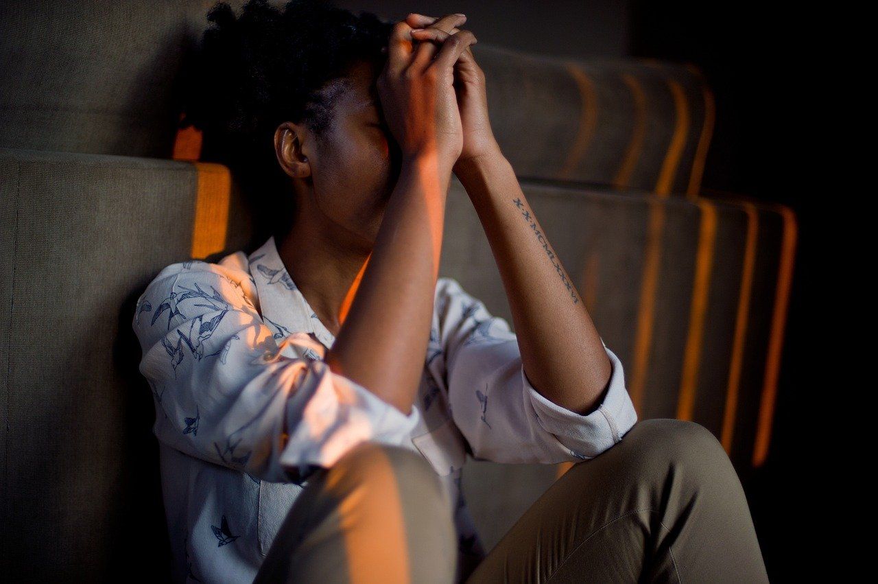 A woman sits on the floor, her head resting against her hands.