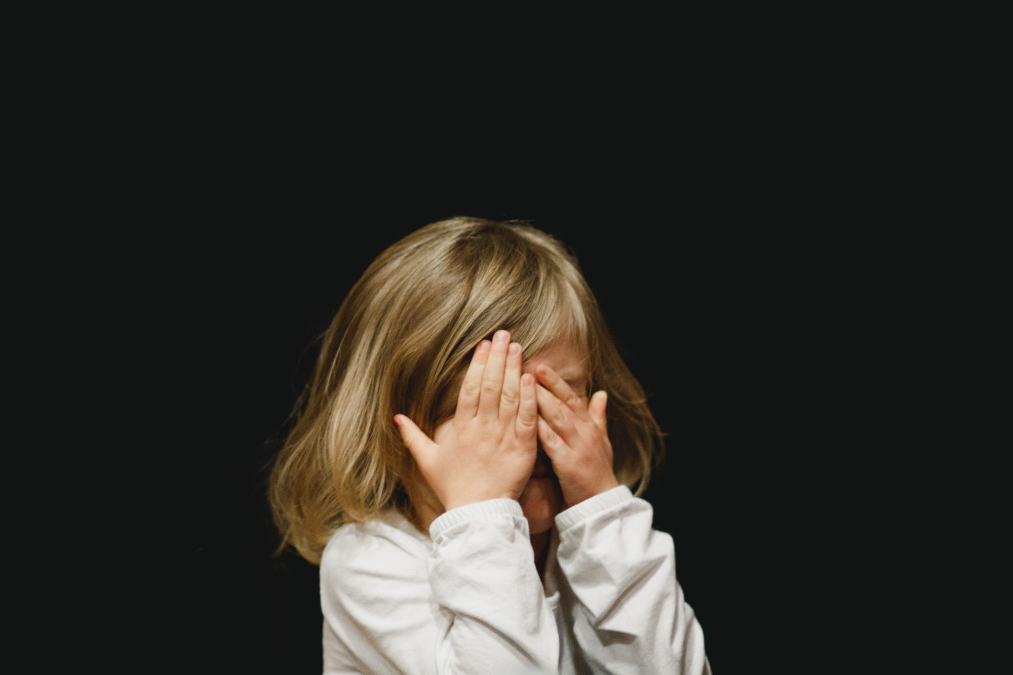 A child hides their face behind their hands