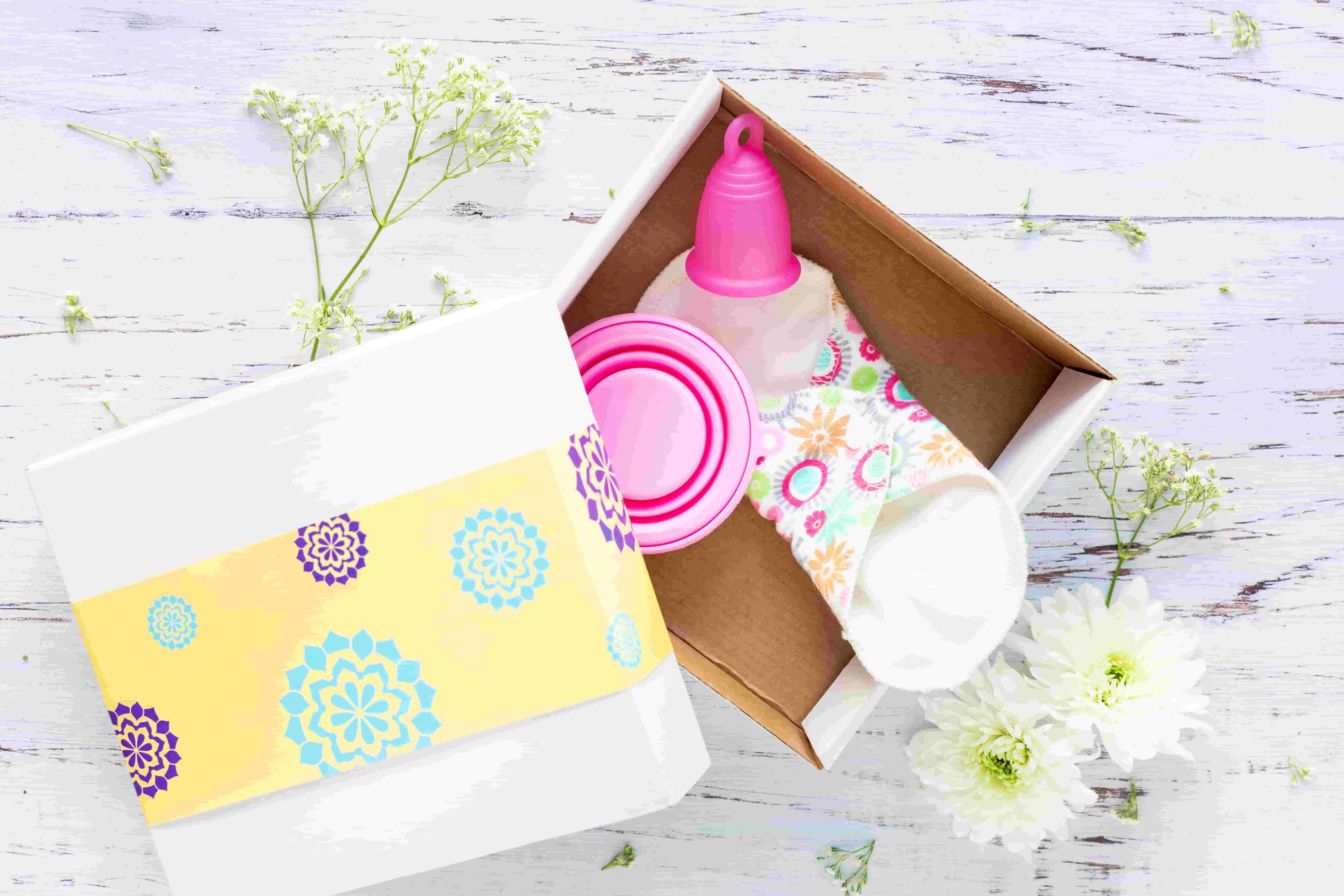 A box sits open with a reusable menstrual cup and pad within it