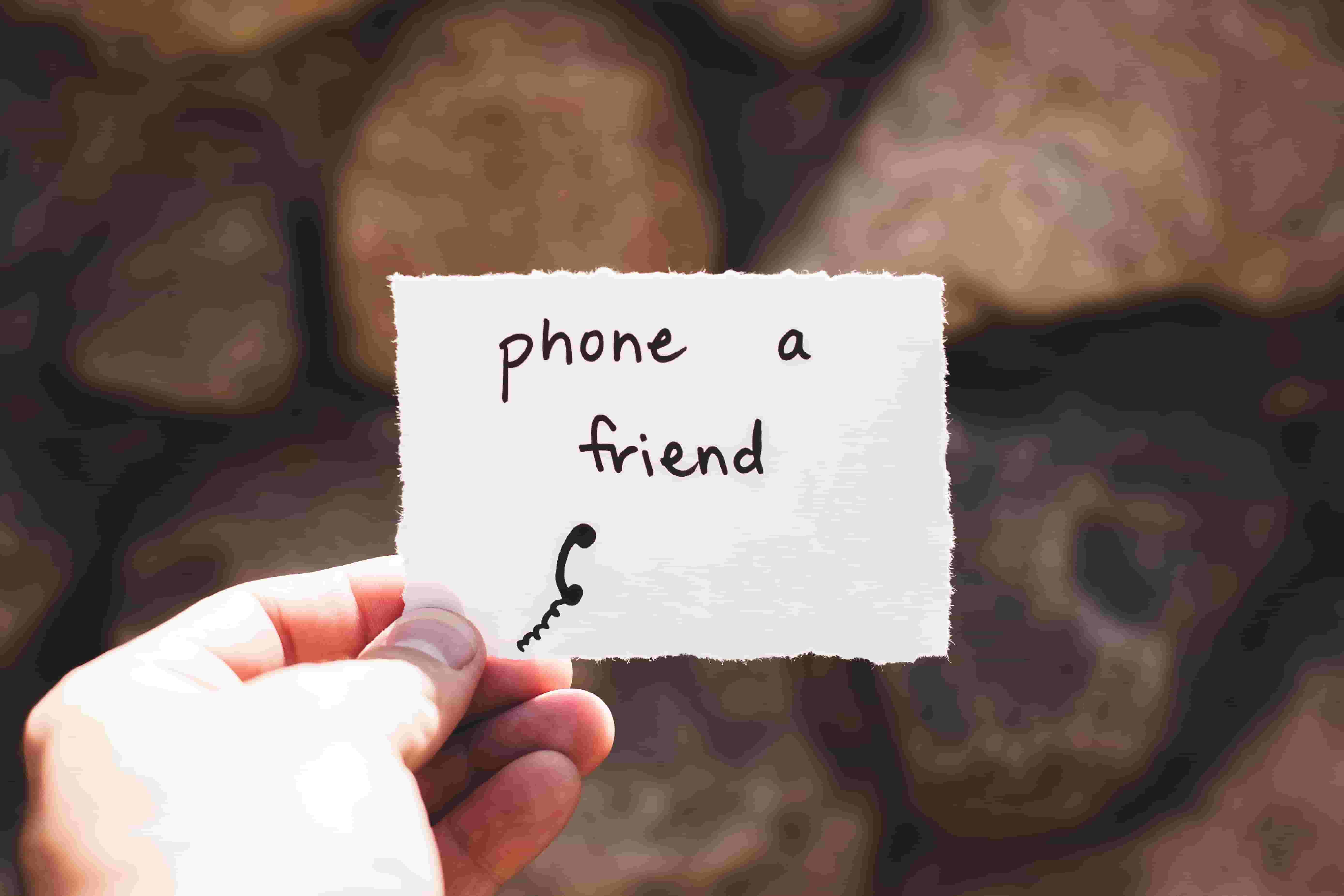 A person holds a piece of paper with 'phone a friend' written on it