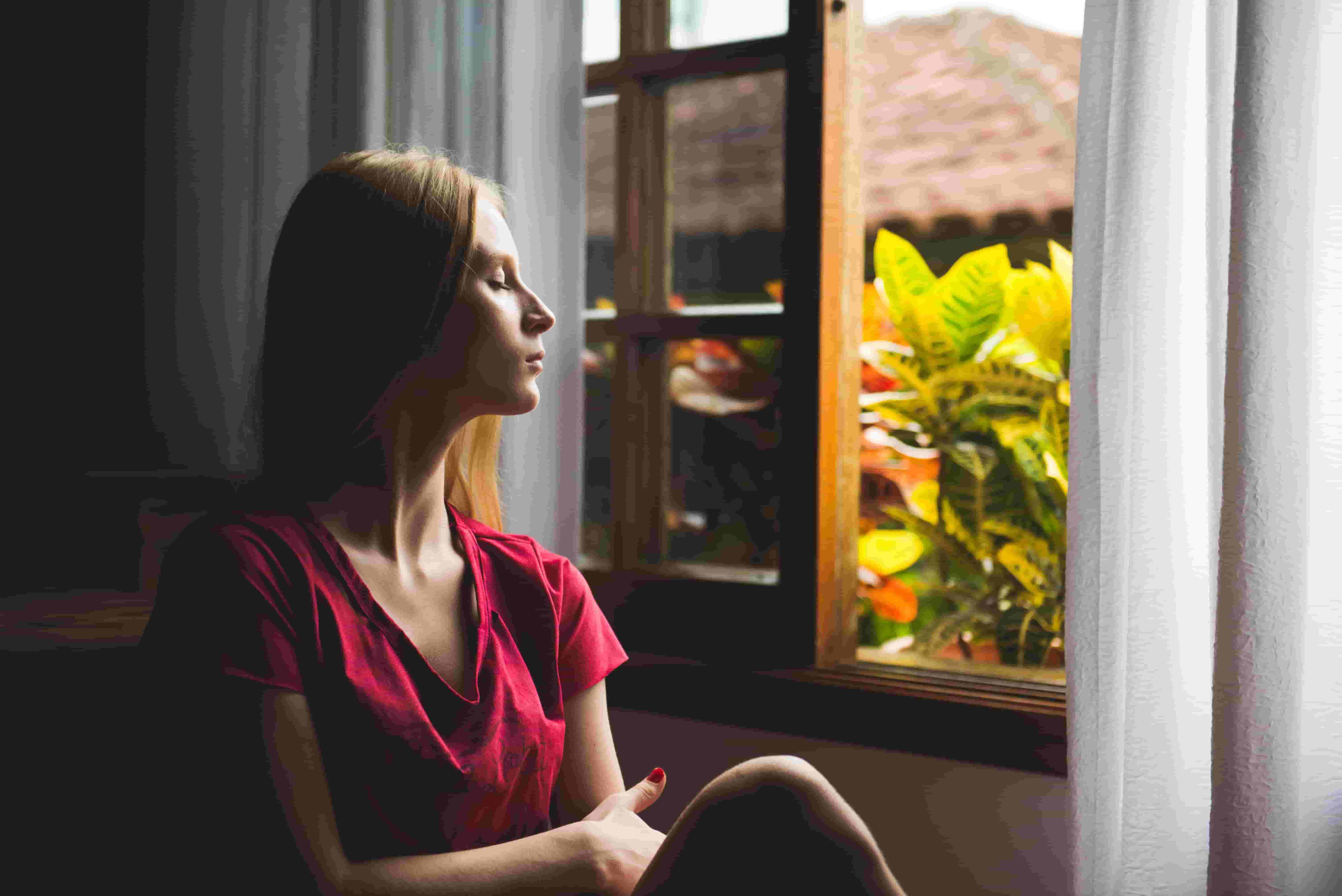 A woman sits by an open window, practicing mindfulness