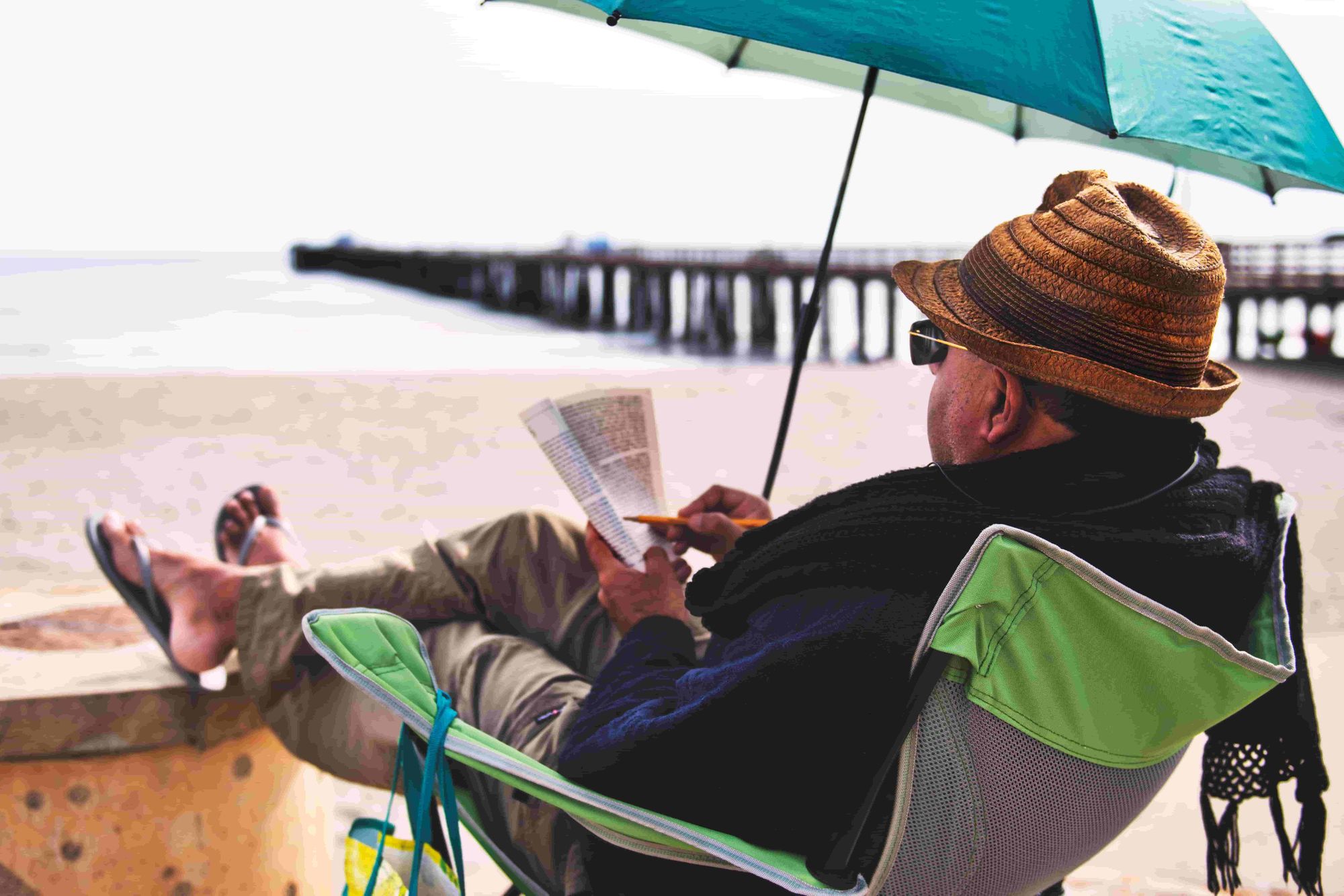 An older man sits on the beach, reading and making notes