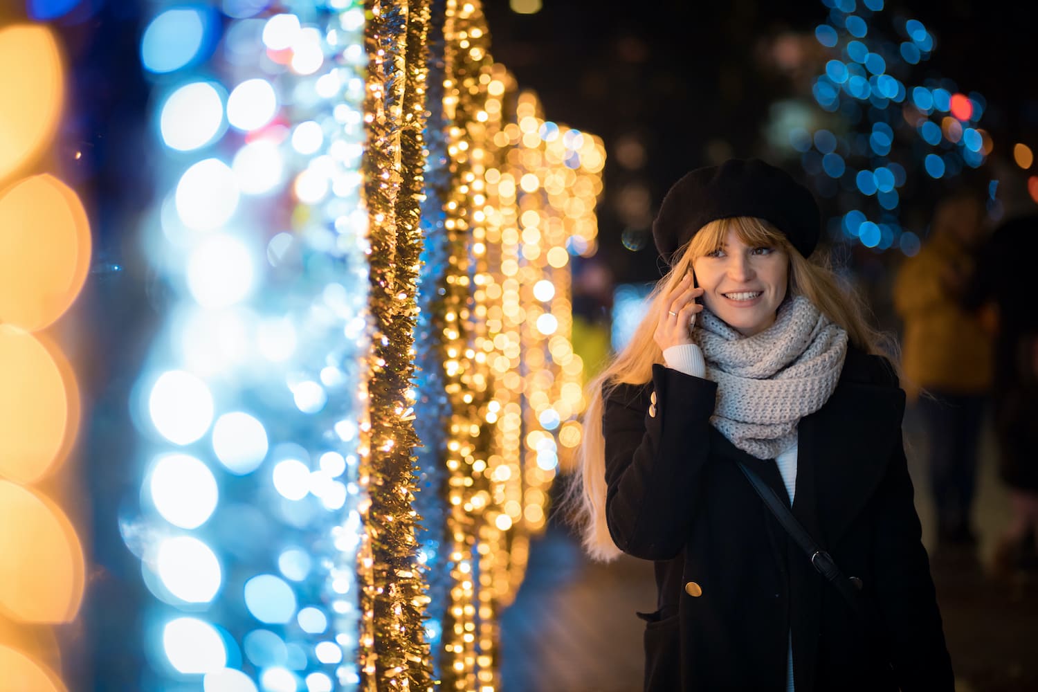 Woman talking on the phone whilst walking next to fairy lights