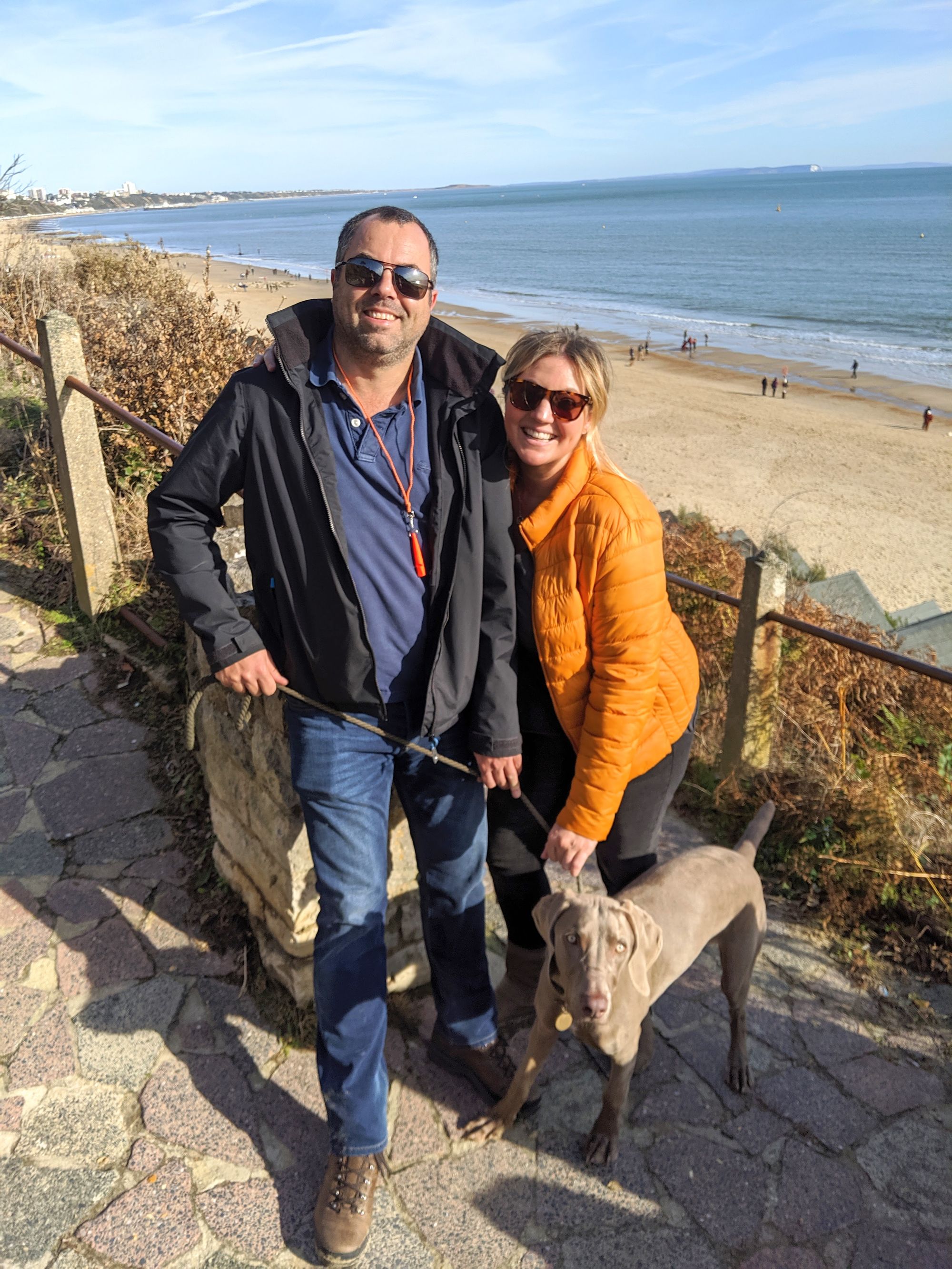 Beth's husband, Beth and their pet dog standing by the beach