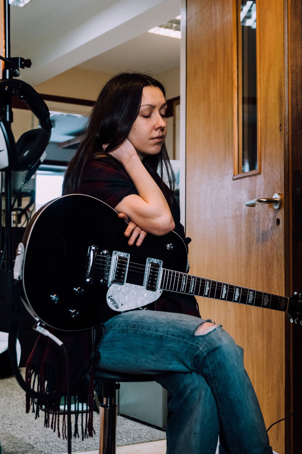 Natalie is sitting on a chair with her guitar, her eyes are closed