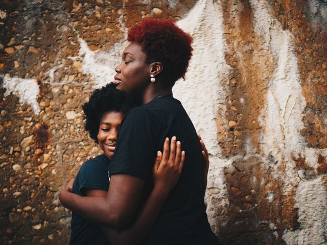 A mother hugs her daughter. Their eyes are closed.