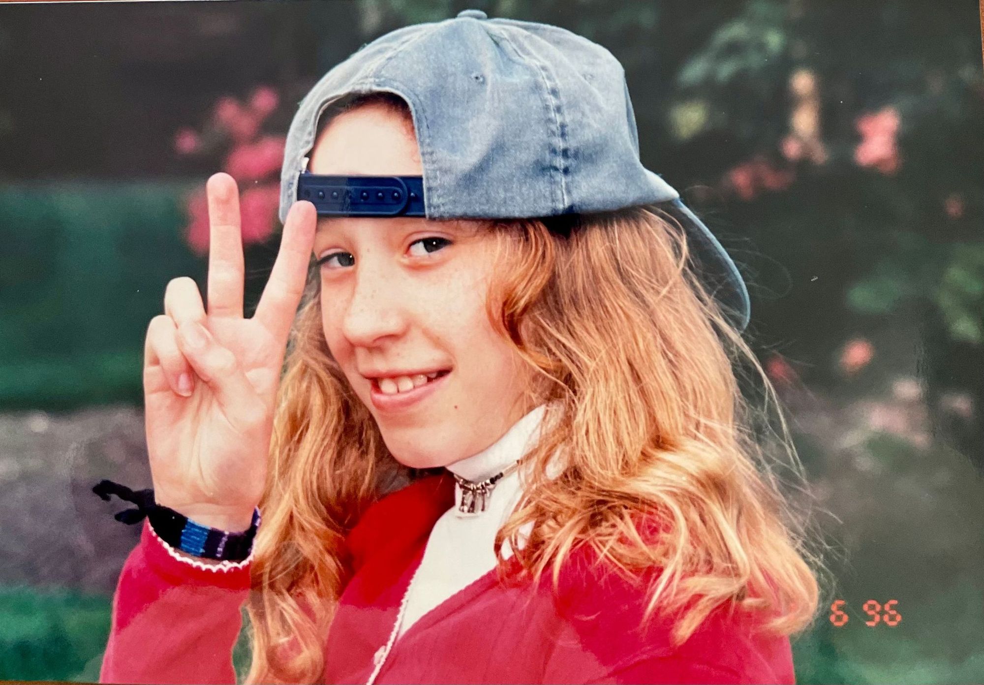 An old picture of Kat at 10-years-old wearing a backwards baseball cap and giving a peace sign to the camera